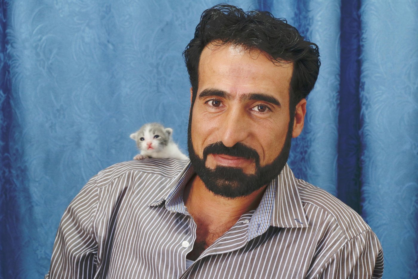 Hashem, 38, a Syrian refugee who lives in Lebanon
Cats’ names: Zaynoun and Zannoun (referred to a Syrian series he used to watch it)
“I love cats since I was very young, but I encountered an incident which made me take the decision to raise cats. Once I was about to drive my work car at night, and I heard a cat meowing, she didn’t stop meowing. I got off the car, and I saw my son, *Ahmad, attached to one of the tires, so I carried him, and took him home. The cat was warning me that something is wrong, she saved my son, and since then I always raise cats.
I used to have 12 cats here in Lebanon, but as we live in the mountains, the hyena ate most of them, only 5 are left now.
I love them like my children, I am very affectionate with them. It is something I can’t explain in words, I love taking care of them, feeding them, and cleaning them.
I consider it a charity deed, God rewards us by taking care of the cats.
They complete my life, whenever I miss anyone of them, I go and look for them.
They always follow me, and sit around me. They are a part of my family, they make me feel better emotionally.
If I go back to Syria, I will give them to someone I trust to take care of them, I don’t think I would be able to take them with me to Syria, crossing the borders with them is not easy.”
Photo: Nadine Malli/NRC