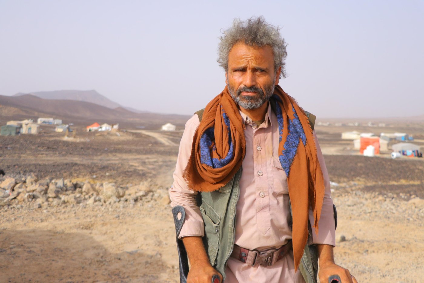 On the 10 April, the same day the first Covid-19 case in Yemen was confirmed, Muhsen Ahmed Mahyoub was fleeing his home. 

Muhsen’s home village of Hareeb was a small and a peaceful one, not far from Sana’a city. On the farm he had inherited from his father, Muhsen kept goats and sheep, and planted corn, barley and wheat. He held on to this quiet life through five years of escalating violence. Even when a landmine took both his legs in 2016, Muhsen still steadfastly continued farming, thanks to the help of his children. The farm was his life, and his only source of income. How would his family eat, if they left?

But on 10 April, one day after a unilateral ceasefire was announced, the war finally forced him to flee.

First came the gunfire in the distance. When it grew closer, Muhsen called his wife and children together, and quickly rounded up the goats and sheep. Around him, other families were doing the same. 

Muhsen hired a small pickup, loading his animals in the back, and struck out for the desert near Marib city. Here, a barren stretch of sandy land has in the last four months become home to 500 families from around Marib and Nihm.
 
It is known as Al-Swaidah camp, though there is nothing to mark it as such: no running water, no toilets, no electricity. It is just there.
 
Muhsen’s family assembled a tent for themselves from iron pipes and plastic sheets. But despite these conditions, Muhsen is just glad to be safe. “We felt we were the luckiest in the world when we arrived.”

Some families still have their goats and sheep with them. Muhsen has sold his animals to buy food and other basic items. “In my village, I used to eat from my farm and sell the rest. But here we are dependent on organizations to help,” he says. “It is true that we can get some food from WFP, but it isn’t enough.”
 
Muhsen is thankful to those organizations which have started to provide mattresses, water and food. But there is so much they still need, including latrines and proper shelter. Storms and floods have damaged several tents in the last few months.

“Before the war, I used to wake up before dawn and walk to the fields and work until ten. Then I would walk to the market to buy some things, and return to have my lunch with family. We sat together in the afternoon to chew Qat and talk—usually about farming. Nowadays, we are thinking all the time how to get food, how to get water and how long we can stay here.”

Muhsen has heard about Covid-19 but doesn’t consider it a threat for displaced people, as they have other, more pressing, worries. None of the displaced people in the camp have been taking any measures against Covid-19.

He has not heard of the ceasefire declaration. He has seen the families still arriving from surrounding areas, fleeing the ongoing fighting. And so far, the news from his hometown is that it has not stopped. “The battles are still ongoing, so we can’t return.”

Photo: Hassan Al-Homaidi/NRC