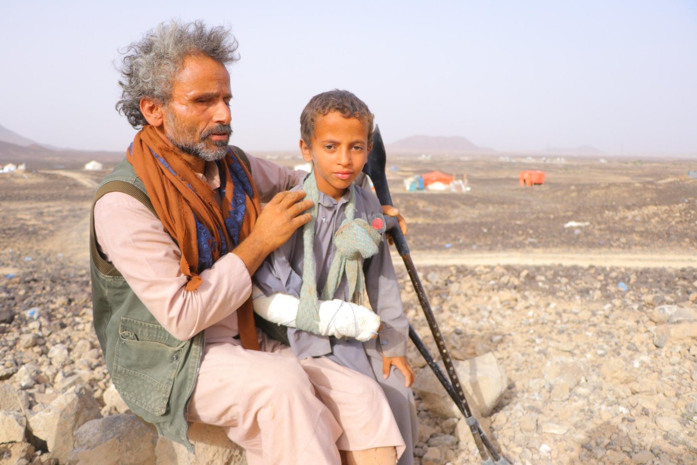 On the 10 April, the same day the first Covid-19 case in Yemen was confirmed, Muhsen Ahmed Mahyoub was fleeing his home.
Muhsen’s home village of Hareeb was a small and a peaceful one, not far from Sana’a city. On the farm he had inherited from his father, Muhsen kept goats and sheep, and planted corn, barley and wheat. He held on to this quiet life through five years of escalating violence. Even when a landmine took both his legs in 2016, Muhsen still steadfastly continued farming, thanks to the help of his children. The farm was his life, and his only source of income. How would his family eat, if they left?
But on 10 April, one day after a unilateral ceasefire was announced, the war finally forced him to flee.
First came the gunfire in the distance. When it grew closer, Muhsen called his wife and children together, and quickly rounded up the goats and sheep. Around him, other families were doing the same.
Muhsen hired a small pickup, loading his animals in the back, and struck out for the desert near Marib city. Here, a barren stretch of sandy land has in the last four months become home to 500 families from around Marib and Nihm.
It is known as Al-Swaidah camp, though there is nothing to mark it as such: no running water, no toilets, no electricity. It is just there.
Muhsen’s family assembled a tent for themselves from iron pipes and plastic sheets. But despite these conditions, Muhsen is just glad to be safe. “We felt we were the luckiest in the world when we arrived.”
Some families still have their goats and sheep with them. Muhsen has sold his animals to buy food and other basic items. “In my village, I used to eat from my farm and sell the rest. But here we are dependent on organizations to help,” he says. “It is true that we can get some food from WFP, but it isn’t enough.”
Muhsen is thankful to those organizations which have started to provide mattresses, water and food. But there is so much they still need, including latrines and proper shelter. Storms and floods have damaged several tents in the last few months.
“Before the war, I used to wake up before dawn and walk to the fields and work until ten. Then I would walk to the market to buy some things, and return to have my lunch with family. We sat together in the afternoon to chew Qat and talk—usually about farming. Nowadays, we are thinking all the time how to get food, how to get water and how long we can stay here.”
Muhsen has heard about Covid-19 but doesn’t consider it a threat for displaced people, as they have other, more pressing, worries. None of the displaced people in the camp have been taking any measures against Covid-19.
He has not heard of the ceasefire declaration. He has seen the families still arriving from surrounding areas, fleeing the ongoing fighting. And so far, the news from his hometown is that it has not stopped. “The battles are still ongoing, so we can’t return.”
Photo: Hassan Al-Homaidi/NRC