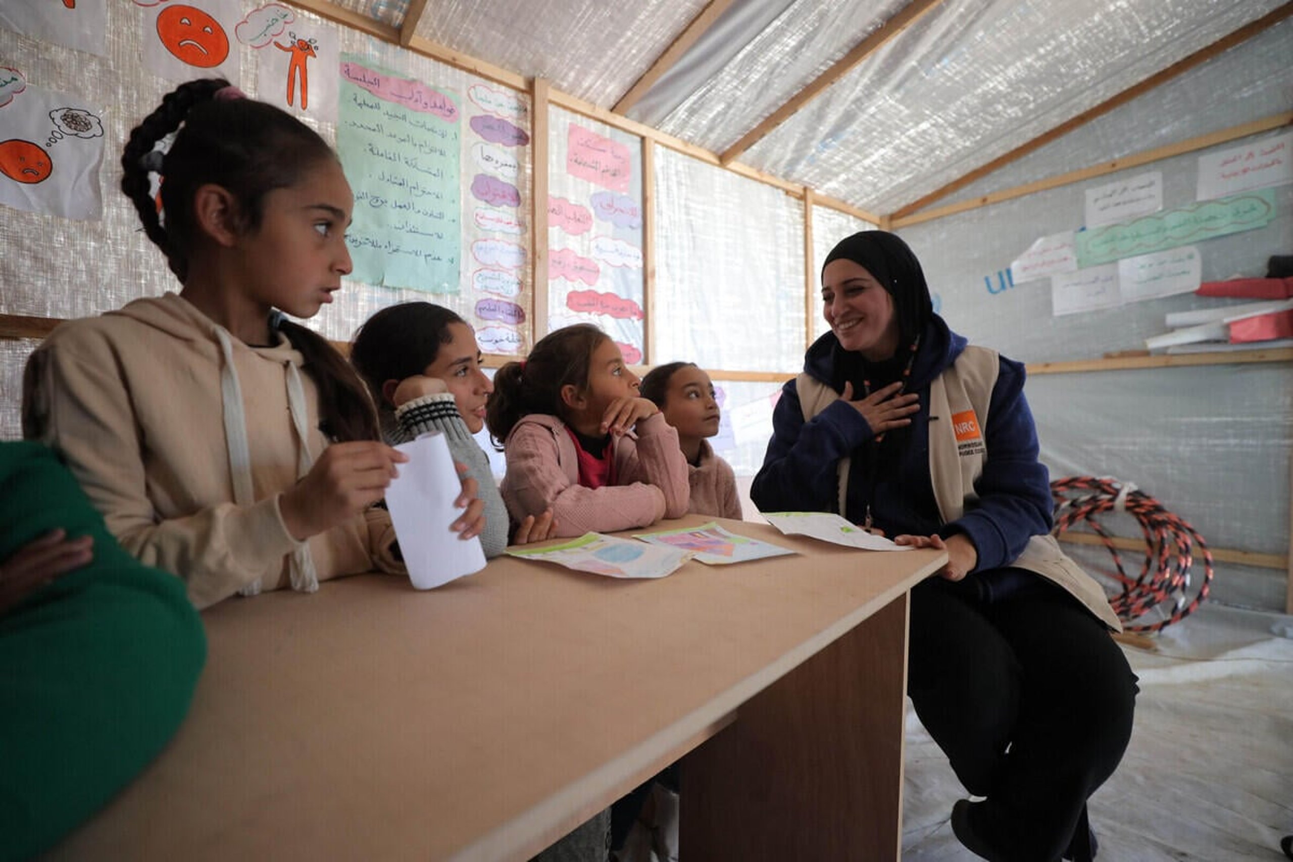 En kvinna från Norwegian Refugee Council sitter tillsammans med fyra flickor vid ett bord i ett provisoriskt klassrum.