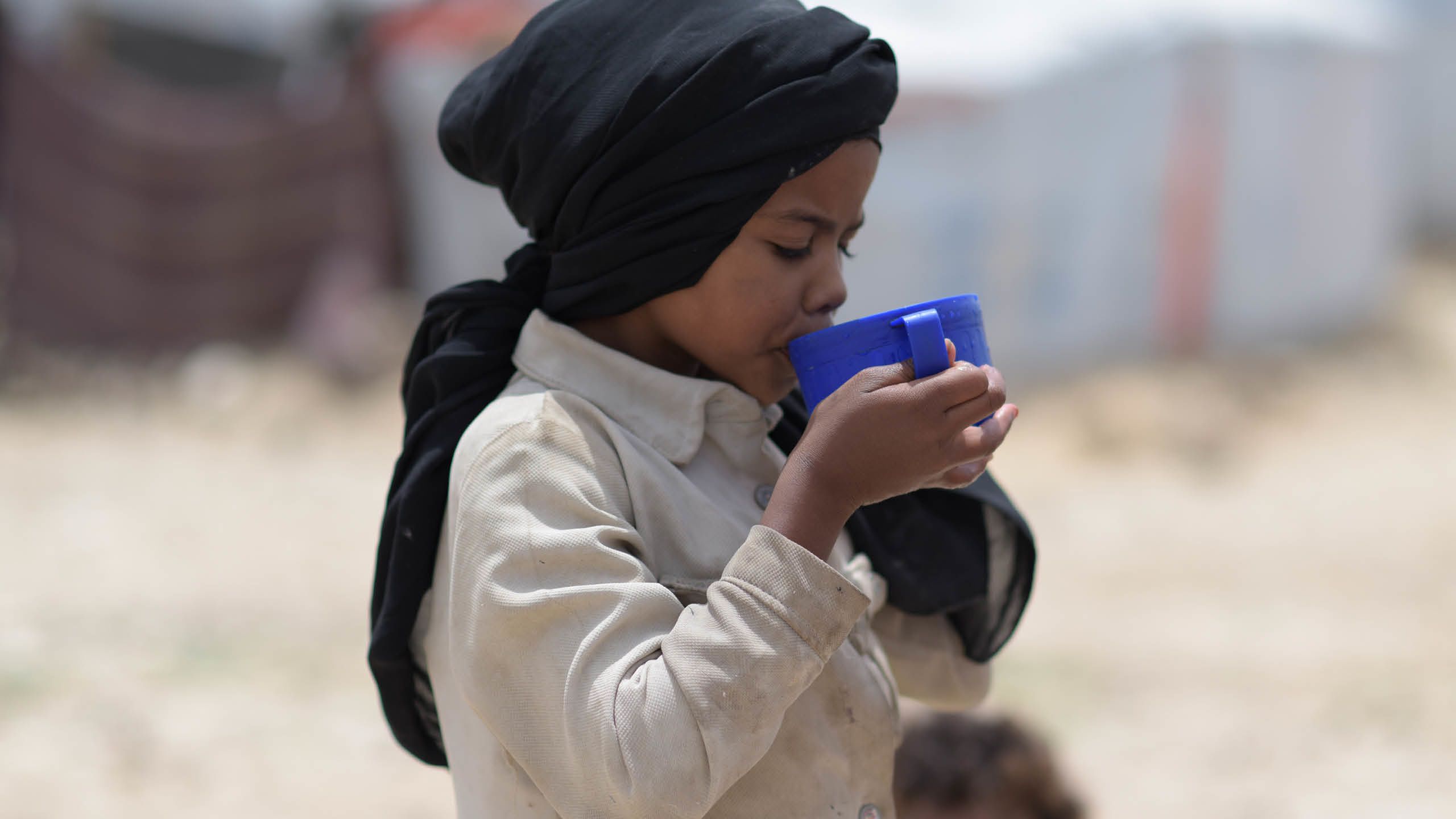 A boy drinking water from a blue cup